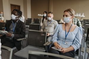 Corporate meeting with participants wearing face masks and taking notes, reflecting COVID-19 safety measures.